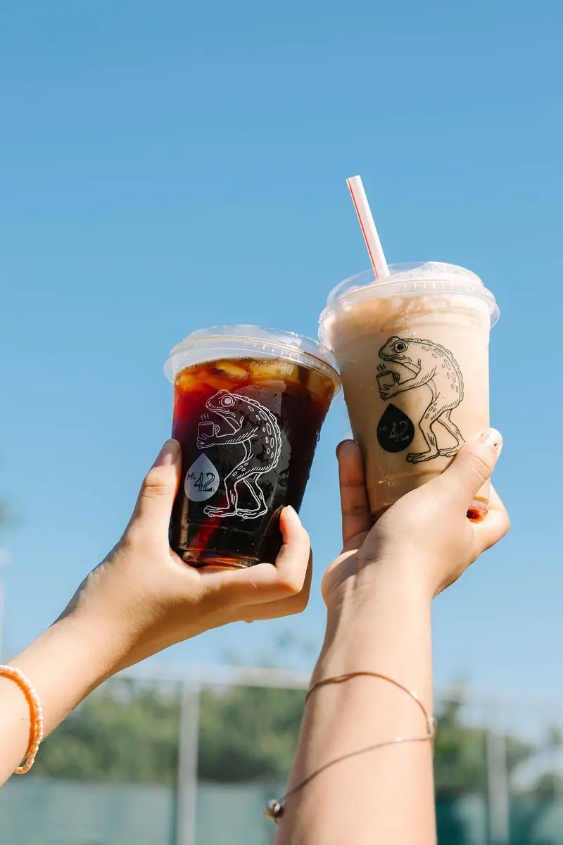 Two Mile 42 iced drinks in Frogman cups held up against a blue summer sky